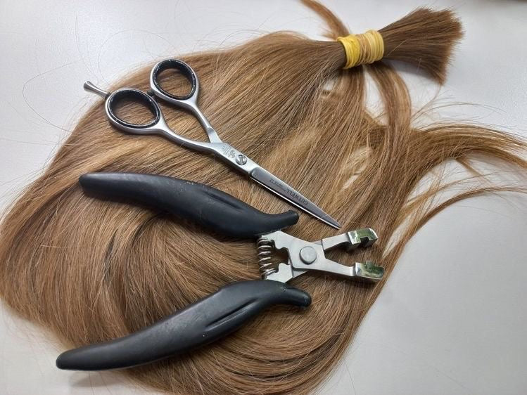 bulk hair, a beautiful honey, blonde dimensional color laying on a table with a pair of shears and a K tip tool to install the hair